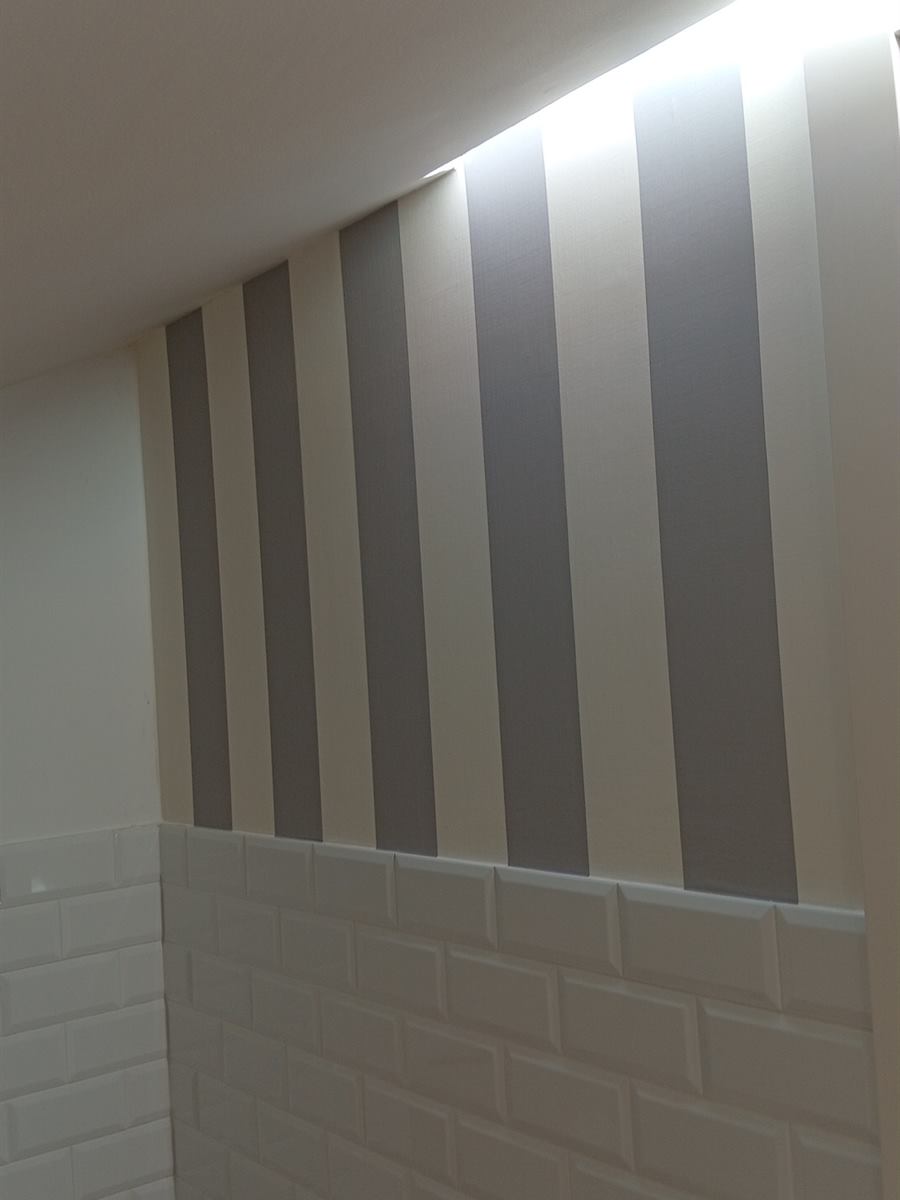 Baño abuhardillado con pared a rayas verticales grises y blancas sobre azulejo blanco